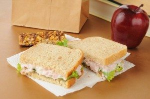 A school lunch with a deviled ham sandwich, apple, granola bar and textbooks